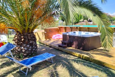 Vasca idromassaggio e zona relax in giardino con piscina fuori terra in legno.